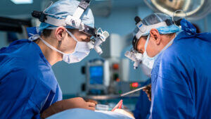 Image of two surgeons in their medical scrubs operating on the abdomen of a patient