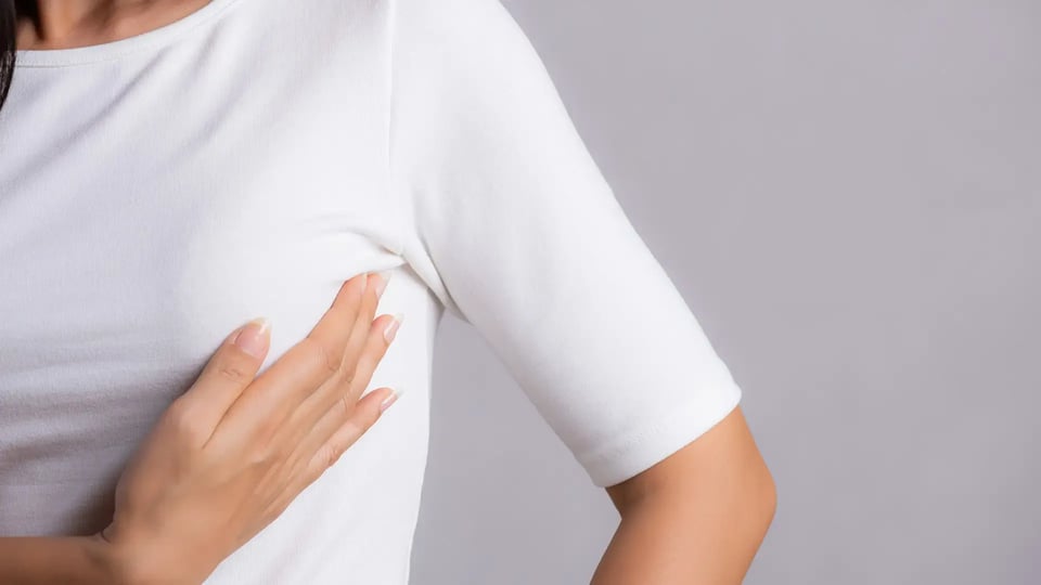 Woman hand checking lumps on her breast for signs of breast cancer on gray background. Healthcare concept_